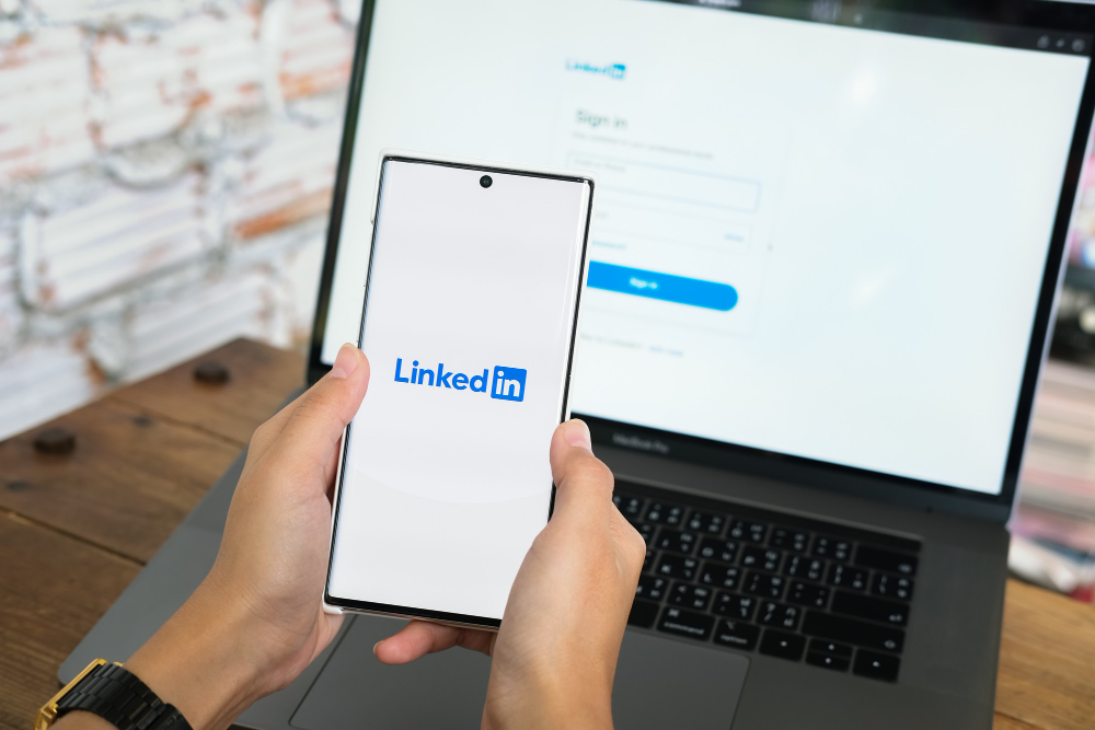 A person holding a phone with the linkedin logo on it.